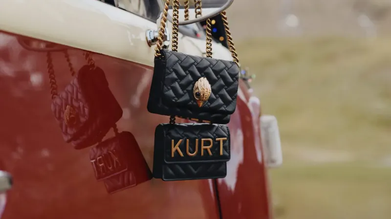Two black quilted Kurt Geiger mini bags with 'KURT' embroidery hanging from a red car's side mirror.