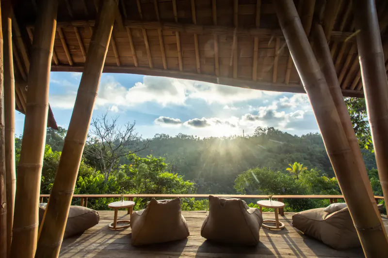 Bamboo pavilion in Buahan Bali with bean bags on deck overlooking lush green hills and sunset