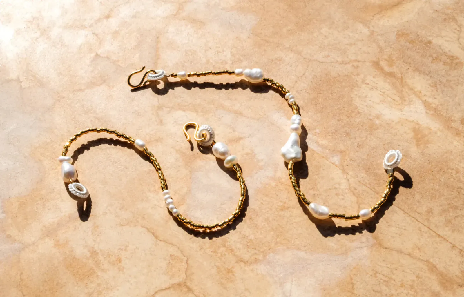 Two gold beaded bracelets with white pebble and loop pearls on a textured surface, Pebble & Loop.