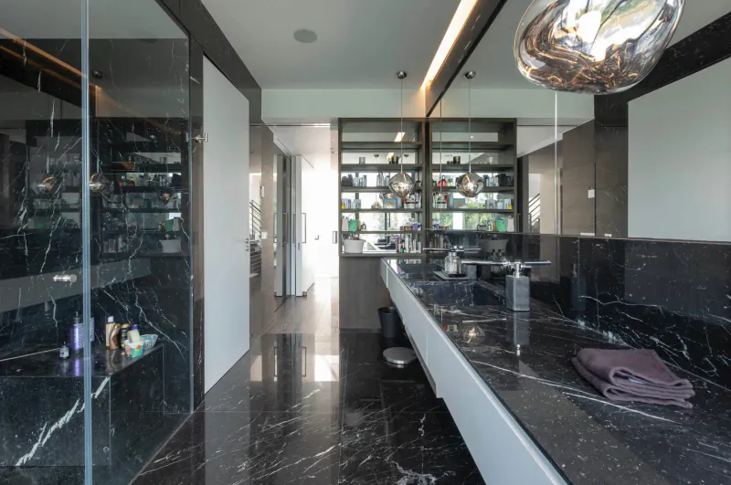 Modern black marble bathroom with white counters, glass walls, shelves of products, and pendant light in Glasshouse by the Lake gallery.