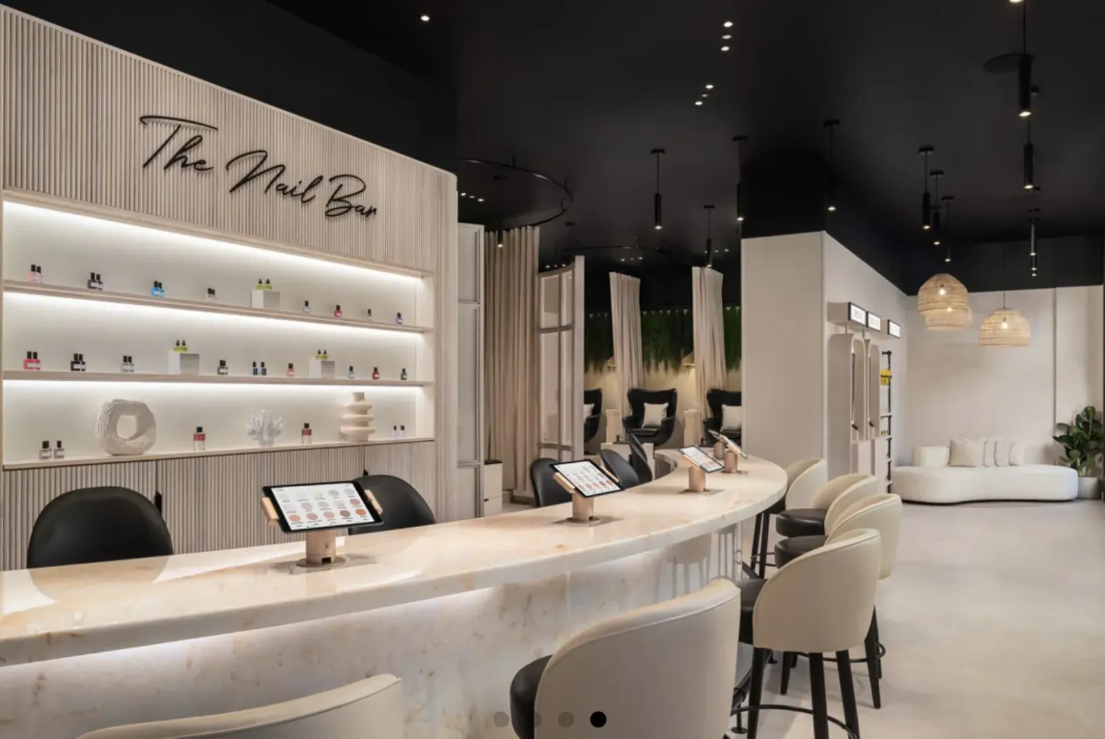 The Nail Box luxury nail salon interior with curved marble reception counter, tablet stands, nail polish shelves, and pedicure chairs.