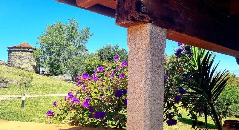 Stone tower on green hill viewed from wooden porch with purple flowers and palm plants under blue sky