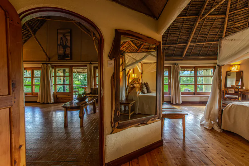 Spacious Chui Lodge bedroom with thatched roof, arched door, large mirror reflecting bed with mosquito net, wooden floors, and window views.