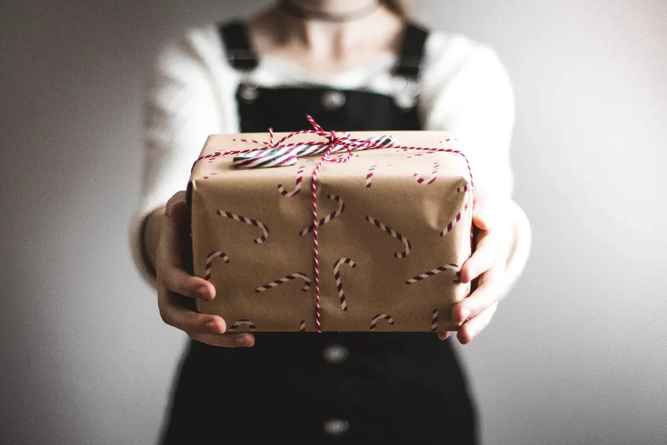 Young woman in white top and black overalls holding a brown gift box with pink striped ribbon