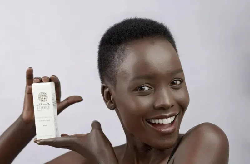 Smiling Black woman with short hair holding up Wild Earth Botanics white oil bottle