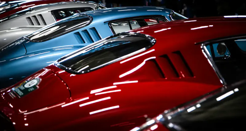 Close-up of classic Le Mans race cars in red, silver, and blue, lined up with glossy vents and curves.