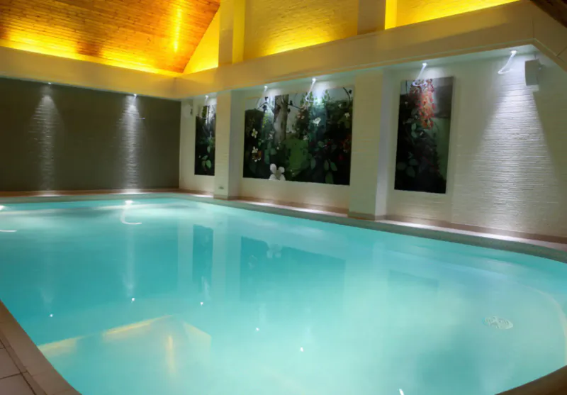Moddershall Oaks spa indoor pool with turquoise water, yellow lighting, wooden ceiling, and leafy wall art.