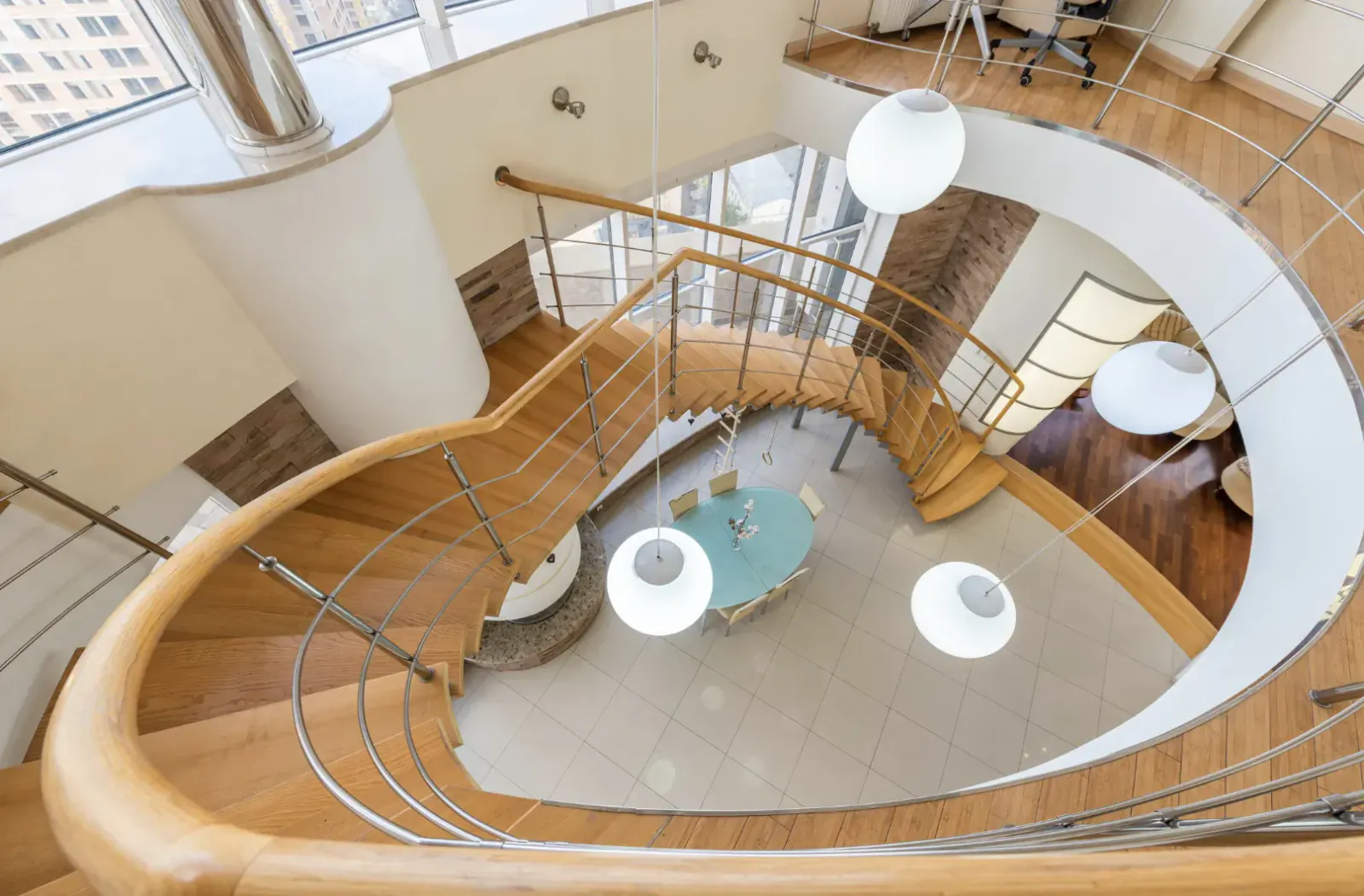 Top-down view of modern curved wooden staircase in high-end loft with white walls, globes, and turquoise table.
