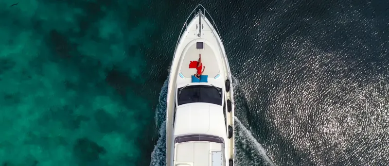 Aerial view of white luxury yacht Hideaway Majesty speeding on turquoise ocean waters with white wake trail