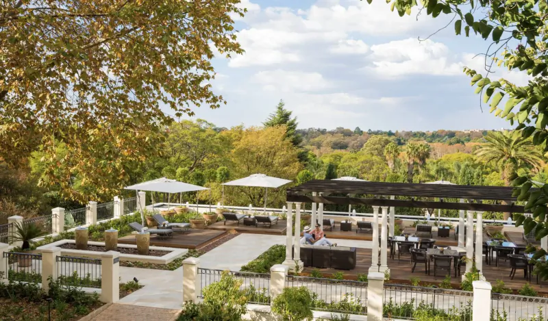 Aerial view of Four Seasons Hotel The Westcliff terrace in Johannesburg, with lounge seating, umbrellas, and autumnal gardens overlooking the city.