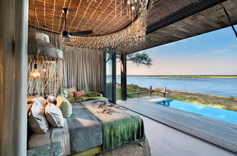 Luxurious Lolebezi safari suite with thatched ceiling, draped bed, open doors to infinity pool and Zambezi River.