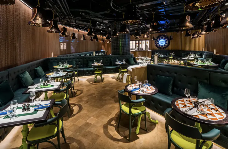 Modern hotel gallery interior blending punk and high-tech: emerald green booths, colorful tables, pendant lights, large wall clock.