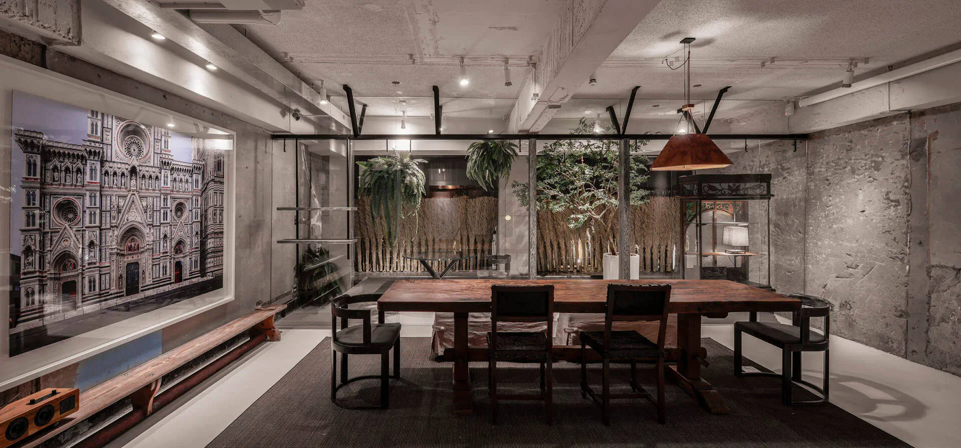 Stylish contemporary restaurant with wooden dining table, black chairs, plants, pendant lights, and cathedral wall art.