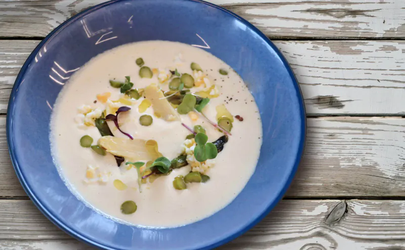 Creamy soup with peas, microgreens, and egg in blue bowl on wooden surface