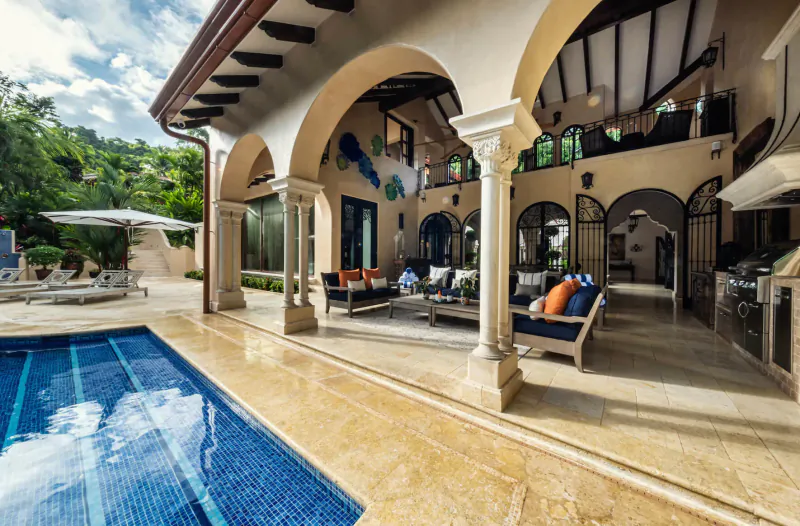 Luxurious modern villa with arched verandas, outdoor seating, infinity pool, and tropical hillside views