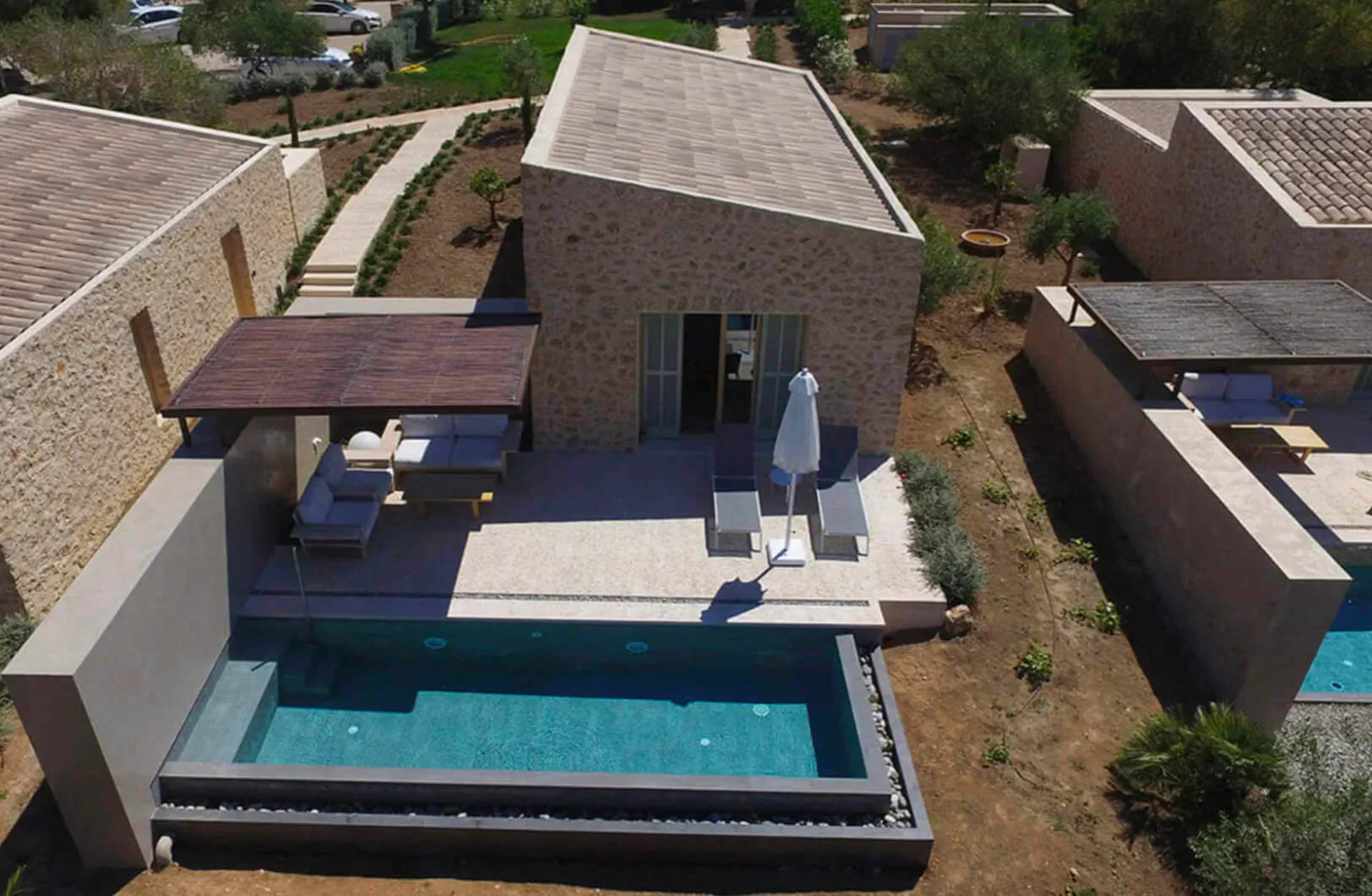 Aerial view of stylish Son Penya hotel villa in Mallorca with infinity pool, terrace, loungers, and umbrella amidst gardens.