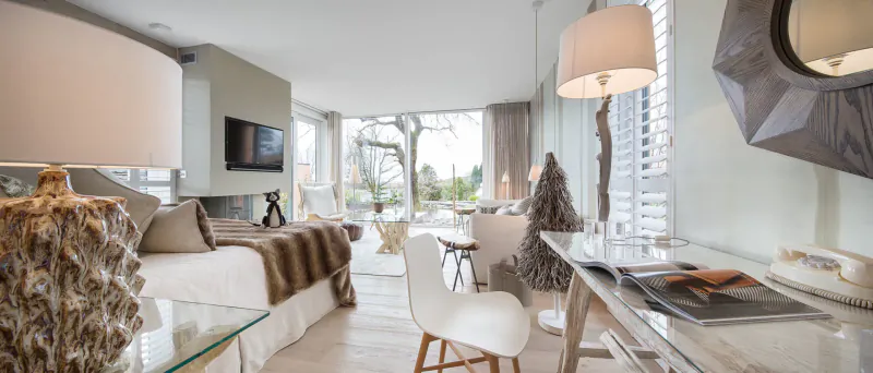 Elegant hotel bedroom at Gilpin Hotel, Windermere: king bed with fur throw, desk, chairs, Christmas trees, window lake view.