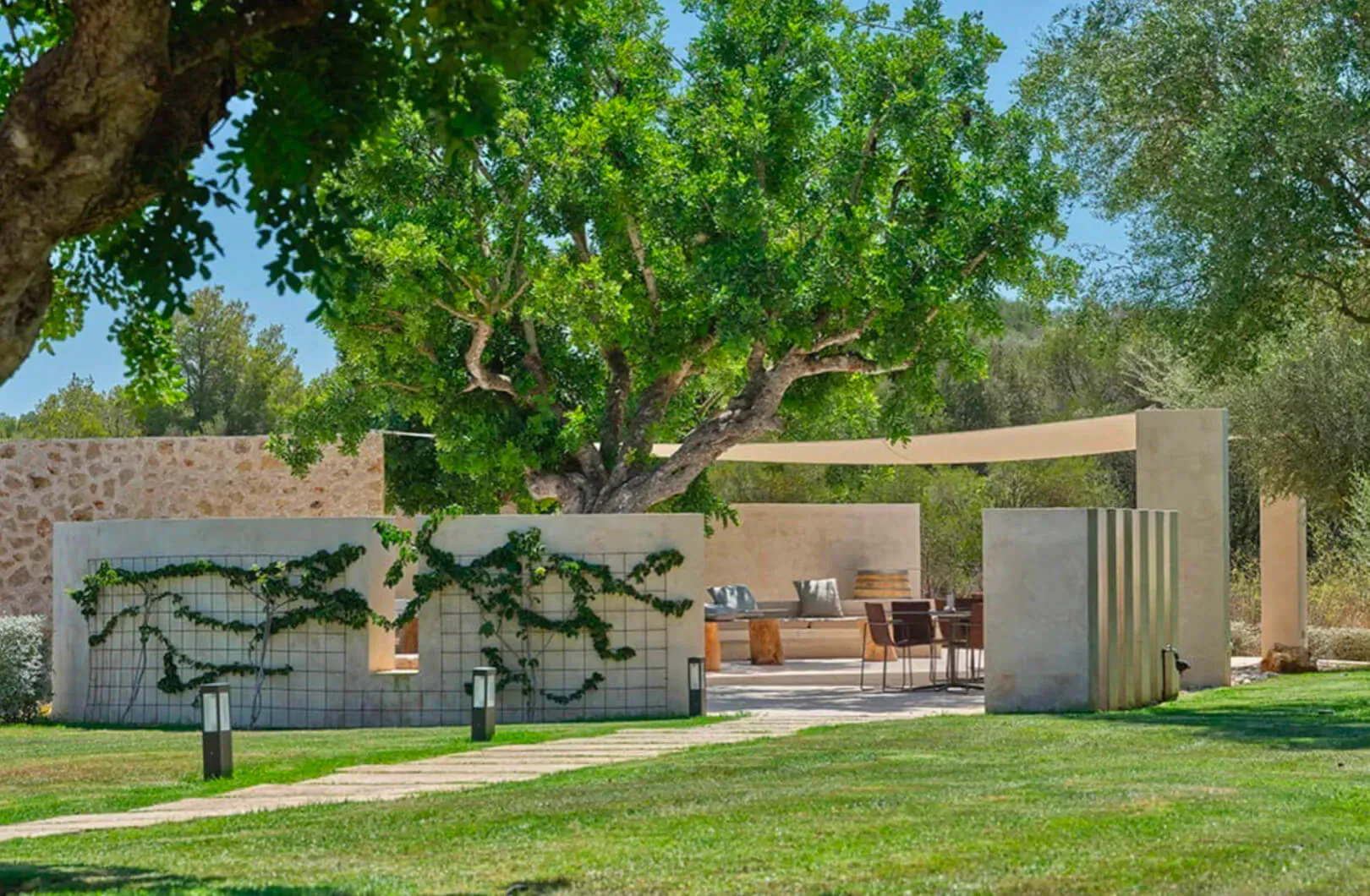 Outdoor lounge at Son Penya Adults Only hotel in Mallorca, with modern beige pergola, olive trees, vines, seating, and lawn path.