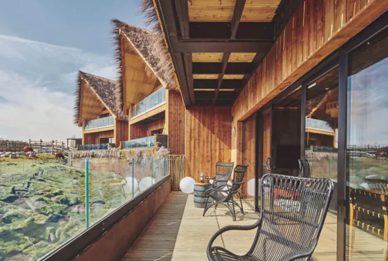 Luxury thatched-roof safari lodge balcony with wicker chairs, overlooking lake and wetlands