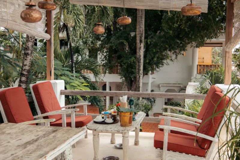 Serene outdoor patio at Kijani Hotel Lamu with red cushioned chairs, rustic table set with tea, brass lanterns, and lush tropical greenery.
