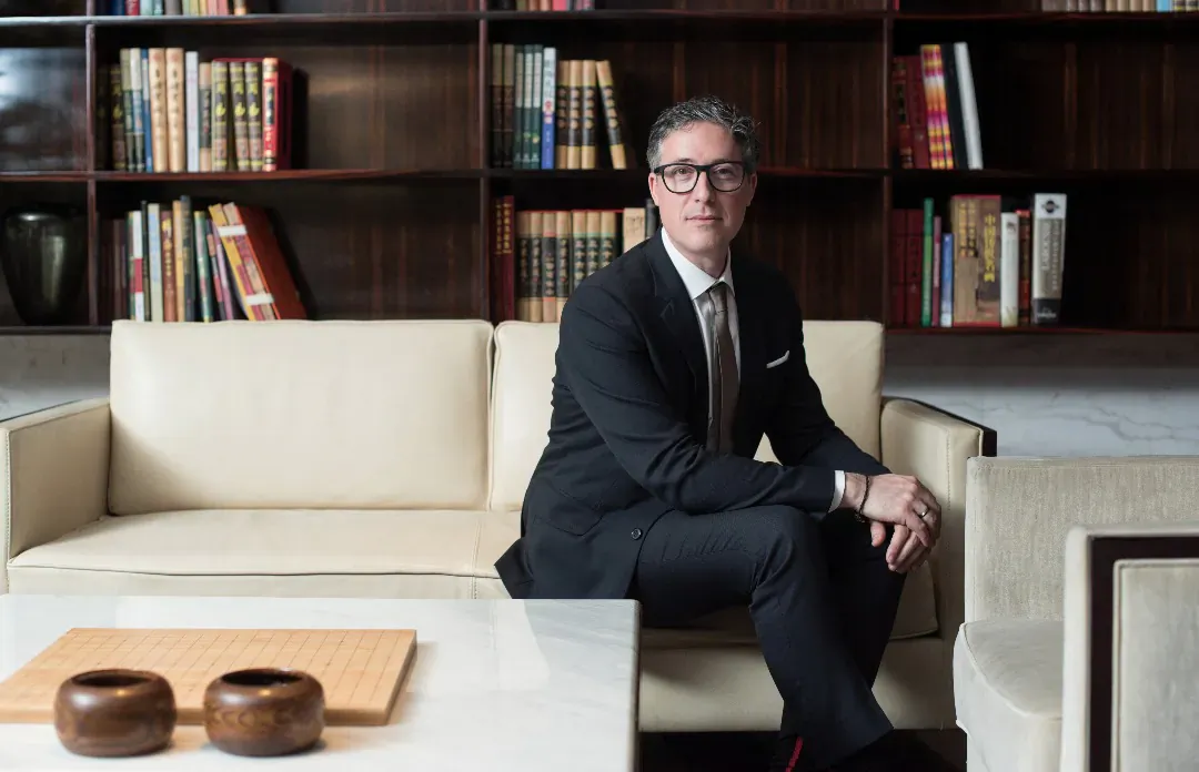 Matteo Atti, CMO of VistaJet, in suit seated on white sofa in wood-paneled library with bookshelves