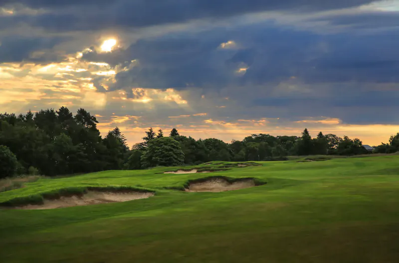 Dramatic sunset over lush green golf course with bunkers and trees at St Andrews resort