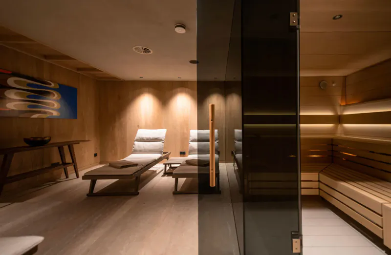 Luxurious wooden sauna in stylish Austrian chalet with lounge chairs, side tables, and abstract wall art.