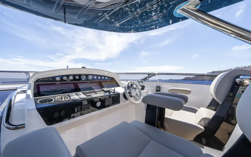 Luxury white yacht helm with dashboard, leather seats, steering wheel, and blue sky over water