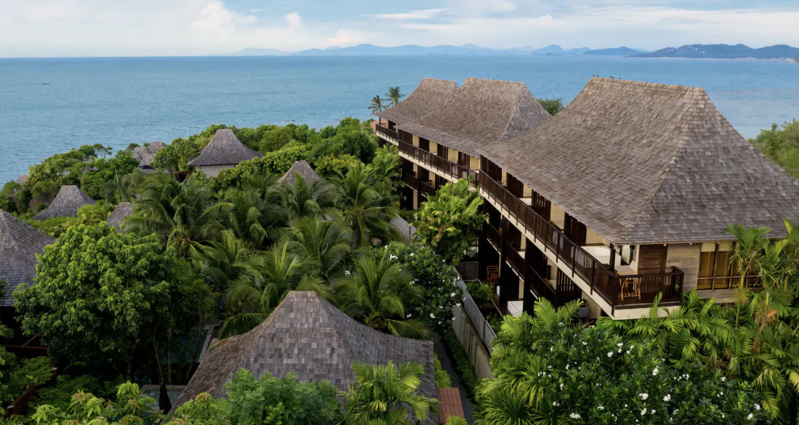 Aerial view of Silavadee Pool Spa Resort's thatched-roof villas nestled in lush tropical greenery overlooking the ocean.
