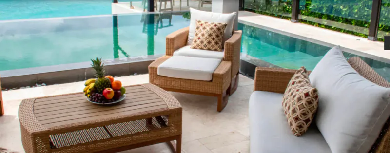Outdoor lounge at Tamarind Hills with wicker chairs, fruit bowl on teak table, infinity pool, and tropical garden view