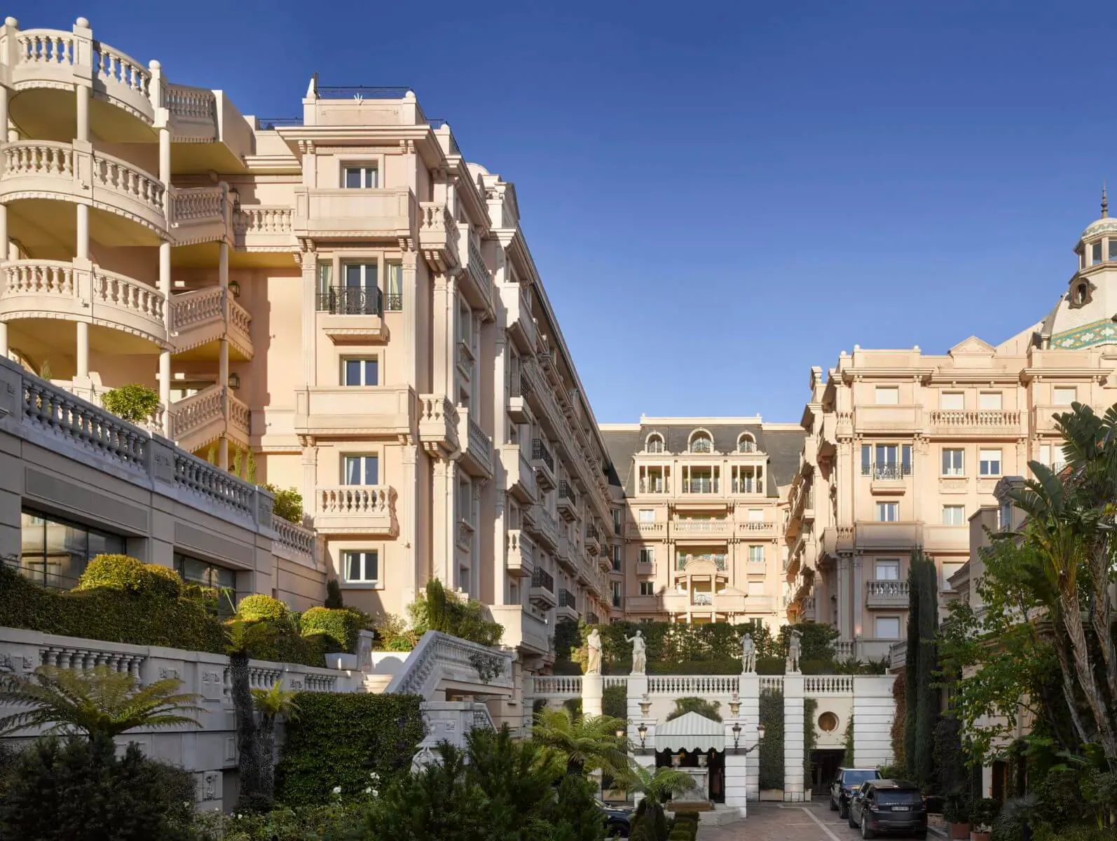 Hotel Metropole Monte-Carlo: ornate beige luxury buildings with balconies, gardens, palms under blue sky