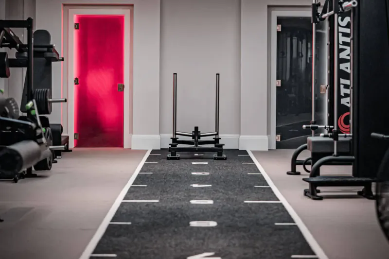 Modern gym interior at The Body Lab with red door, Atlantis machines, sled on black track, and weights.