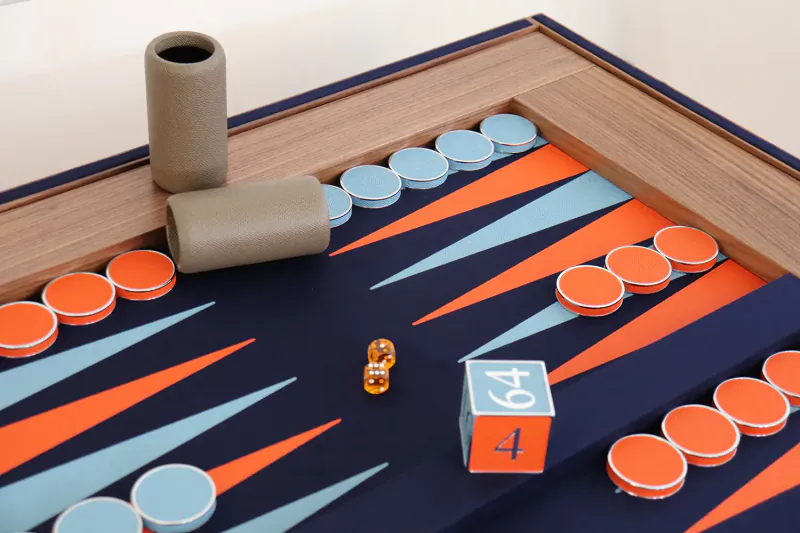 Luxury backgammon board in progress with orange and teal checkers, dice showing 4 and 6, and gray cardboard tube.