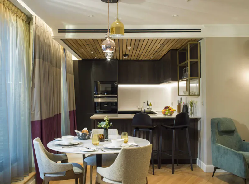 Elegant modern kitchen and dining area in The Guardsman boutique London hotel, with wooden ceiling, pendant lights, set table, and counter with fruit.