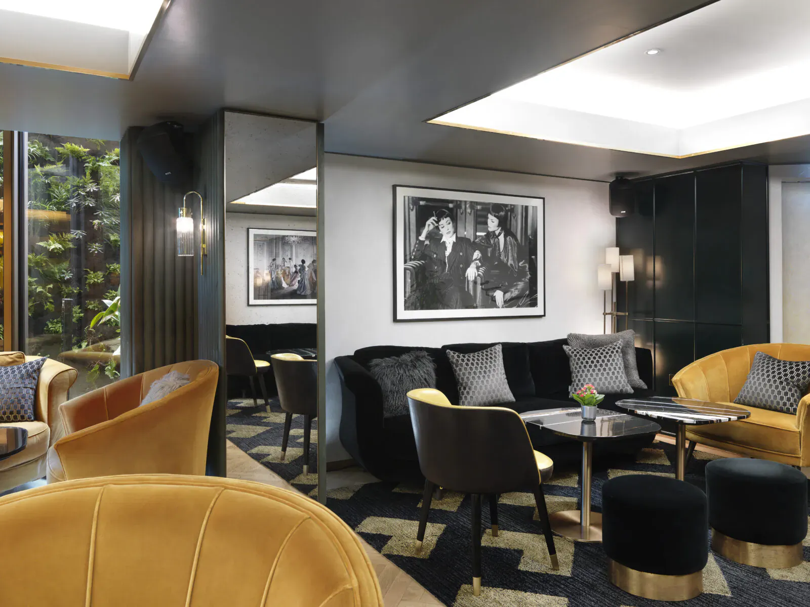 Elegant lounge at The Athenaeum Hotel with yellow velvet armchairs, black sofas, gold accents, mirrors, plants, and black-and-white art.