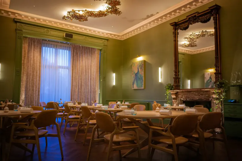 Elegant green dining room with wooden tables and chairs, ornate ceiling, large mirror, abstract painting, and fireplace.
