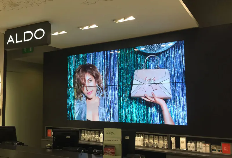 ALDO store interior with large video wall displaying smiling woman holding white handbag amid blue sequins, checkout counter