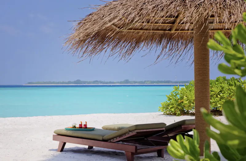 Luxury beach loungers with drinks under thatched umbrella at Amari Raaya Maldives resort, turquoise ocean view