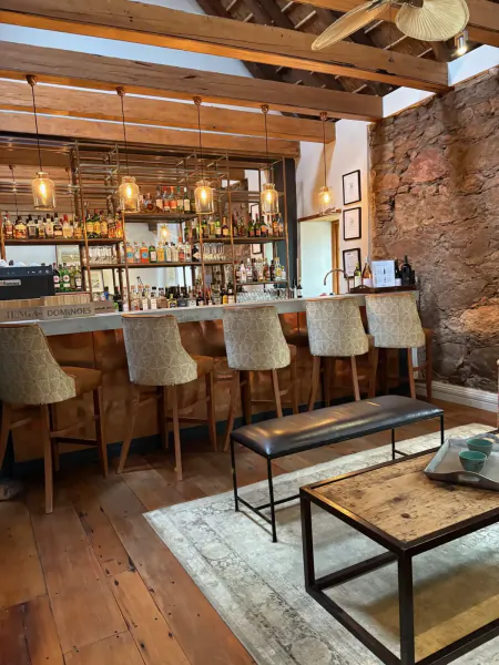 Rustic wooden bar at The Old Rectory with stone walls, pendant lights, barstools, and lounge table on rug