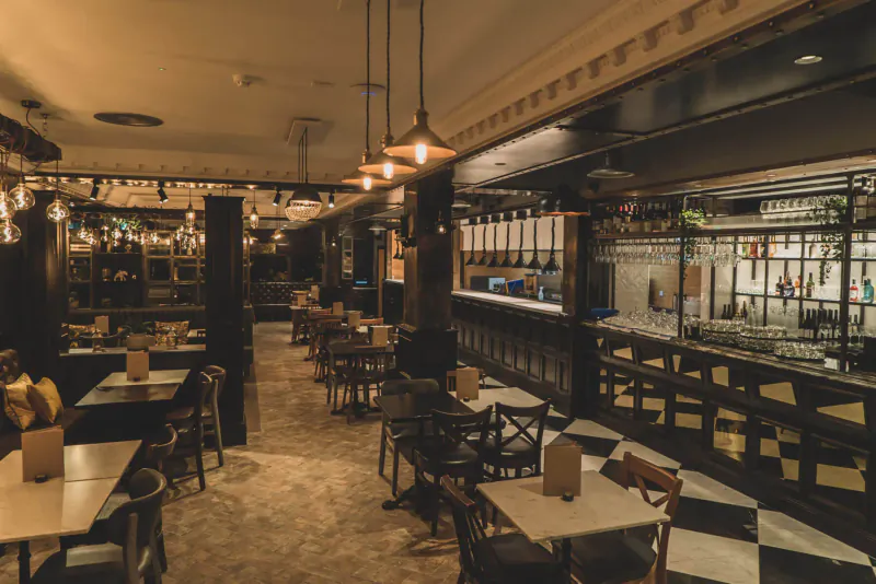 Elegant empty Six by Nico restaurant interior with wooden tables, chairs, and ornate bar.