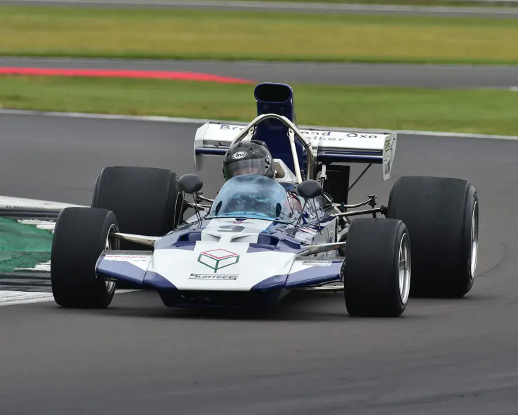 White and blue March Formula 1 racing car speeding on track at London Concours 2024 event.