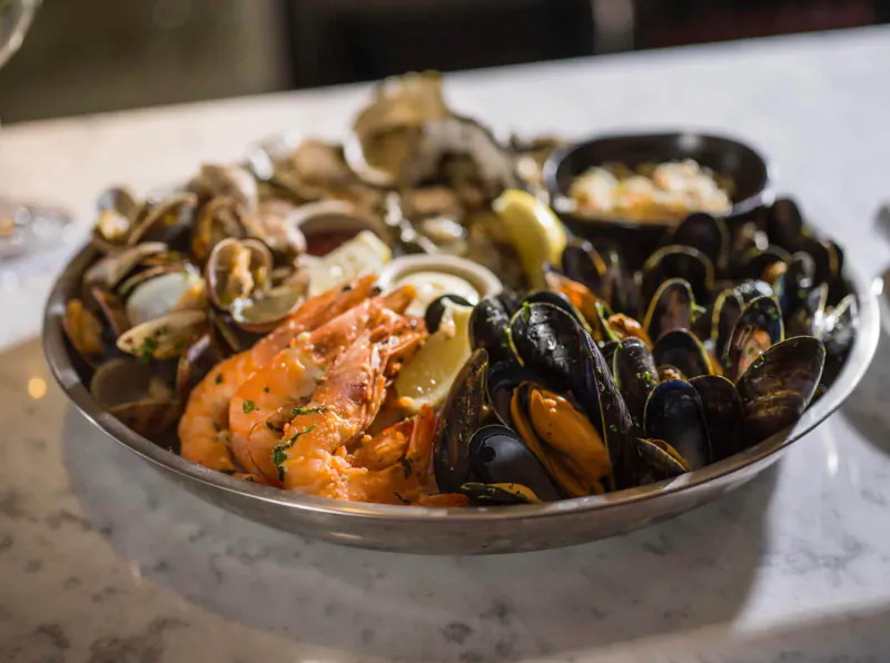Seafood platter with mussels, clams, oysters, prawns, lemon wedges in silver bowl on marble table