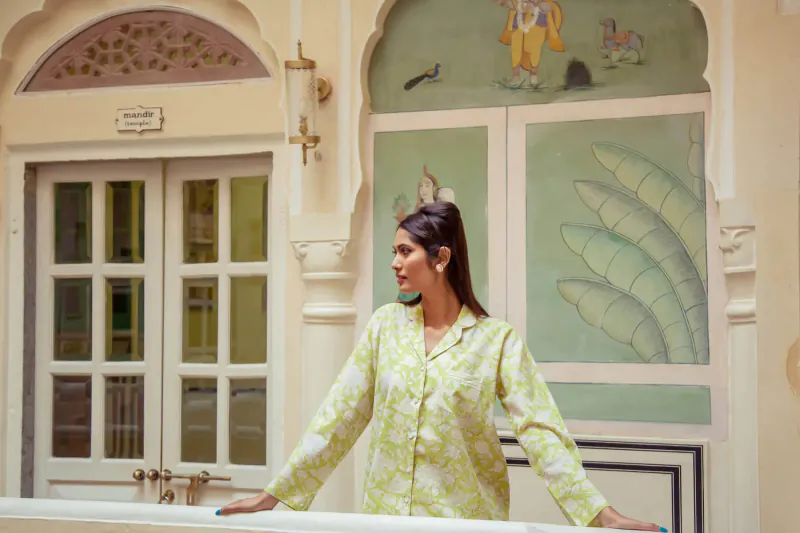 Woman in green floral pajamas poses in front of ornate Indian archway with Krishna mural and peacock motifs