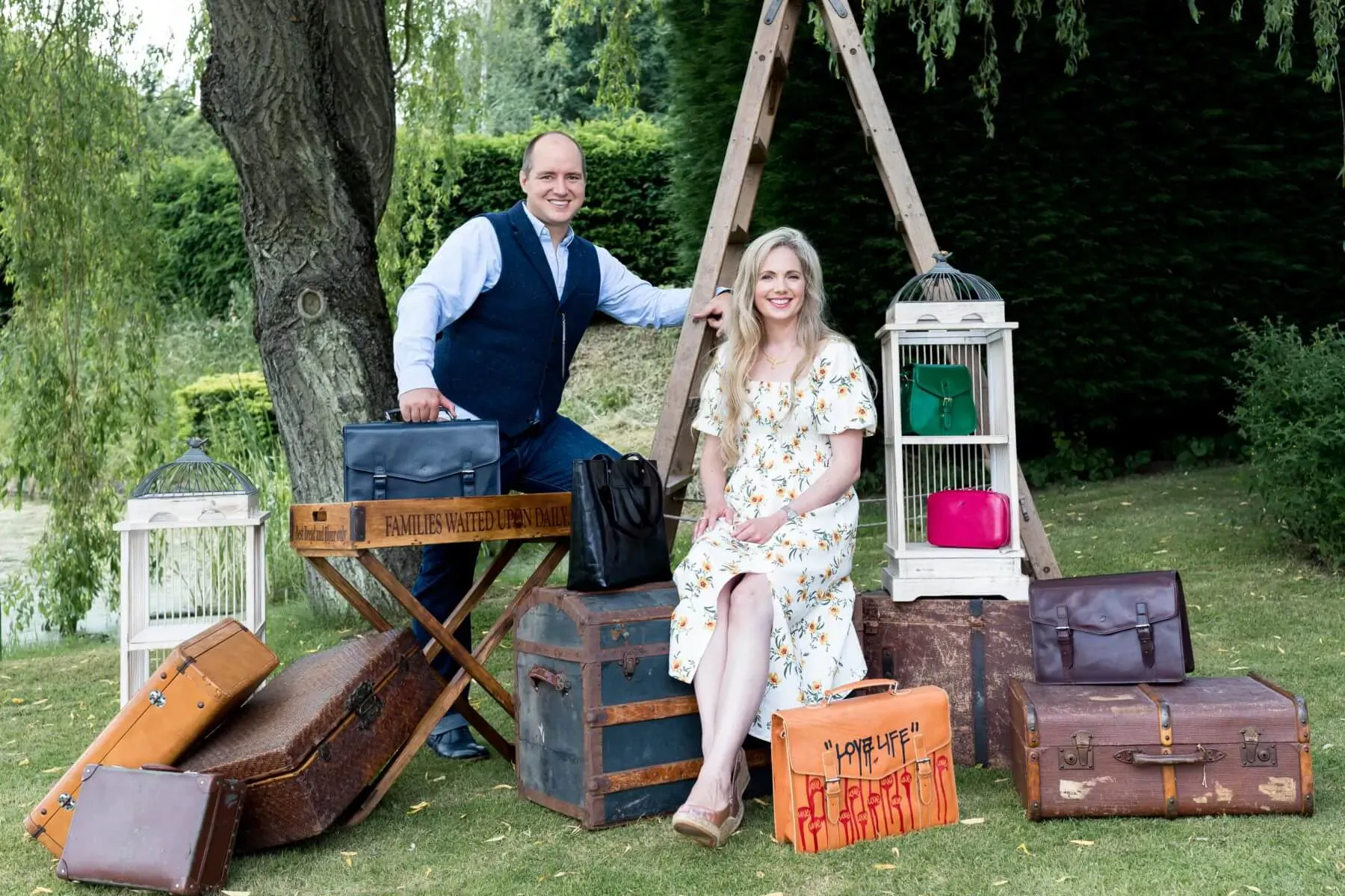 Smiling couple poses with vintage suitcases and bags in lush garden setting for Rufus Country.