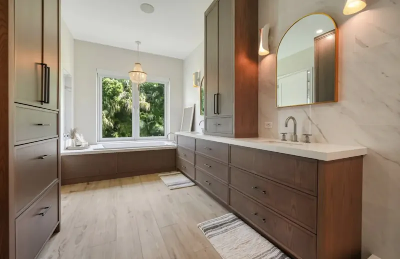 Luxurious walk-in closet with wooden wardrobes, marble vanity, arched mirror, and garden window view.