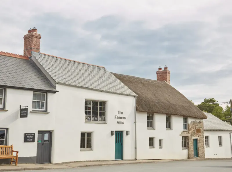 The Farmers Arms pub, a white thatched cottage with green door in Woolsery, North Devon, cloudy sky.