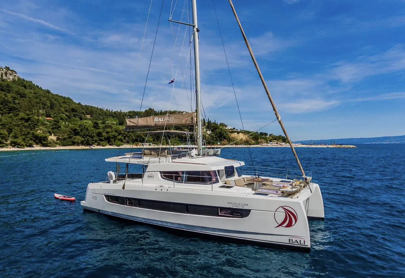 White Bali 4.6 catamaran anchored in calm Croatian bay with hills, castle, red kayak nearby