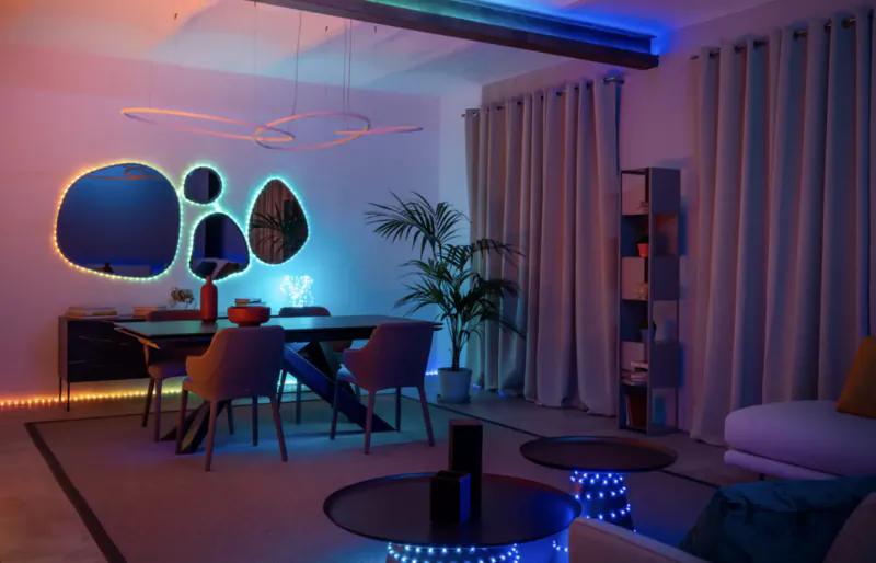 Modern living room with dining table, chairs, plants, and Twinkly Dots LED strip lights glowing blue and purple.