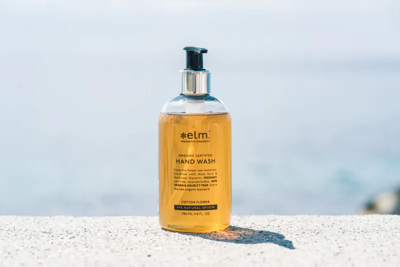 Eimi Elm Organics hand wash bottle on stone ledge by sunny beach.
