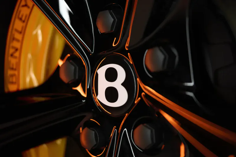 Close-up of black Bentley wheel with prominent white 'B' logo and yellow brake calipers